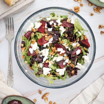 Overhead view of Grilled Beetroot Goat Cheese Salad in a bowl, with roasted beetroot slices, chopped walnuts, and goat cheese in the background.