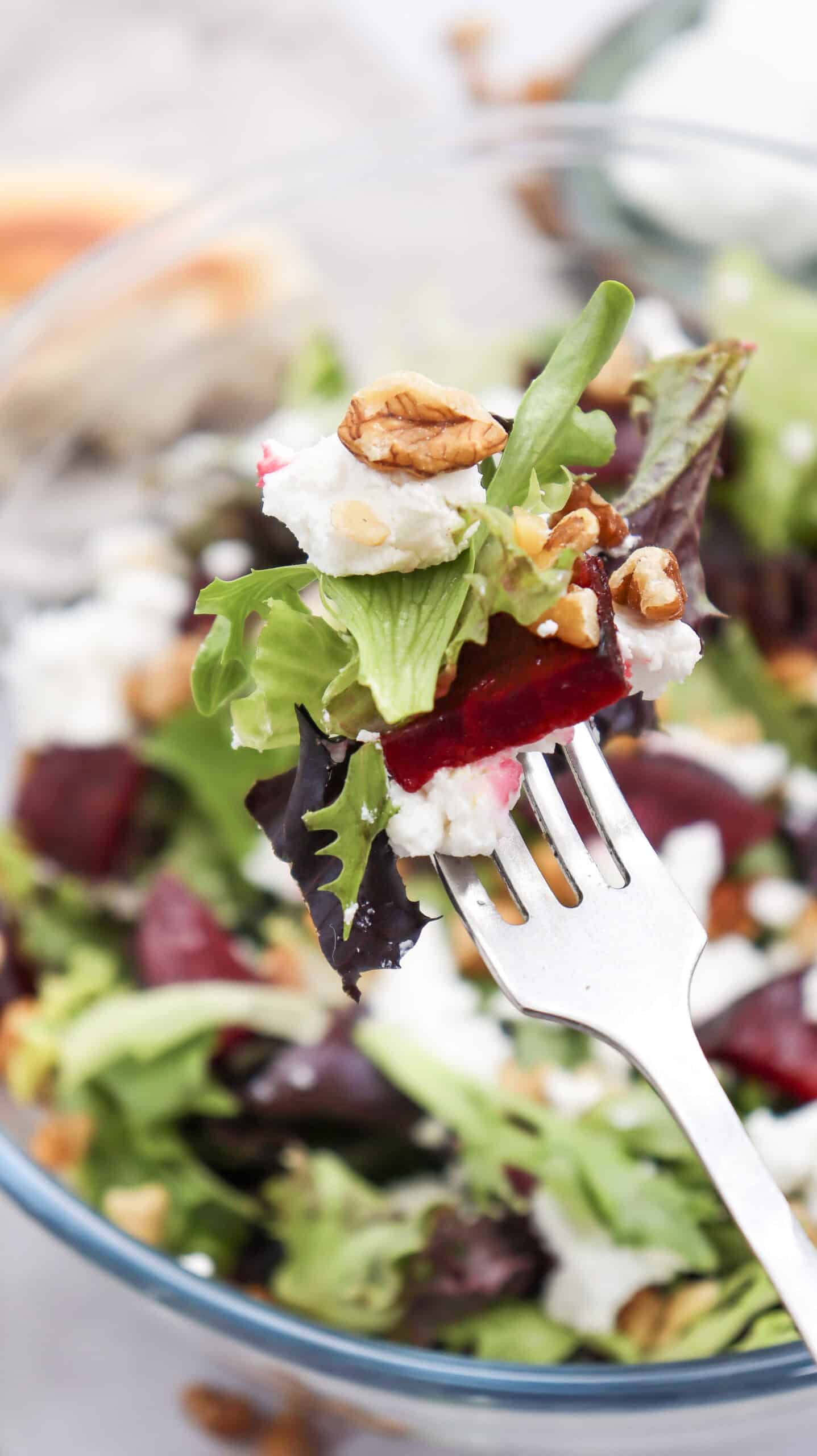 A bite-sized piece of grilled beetroot goat cheese salad being lifted by a fork.