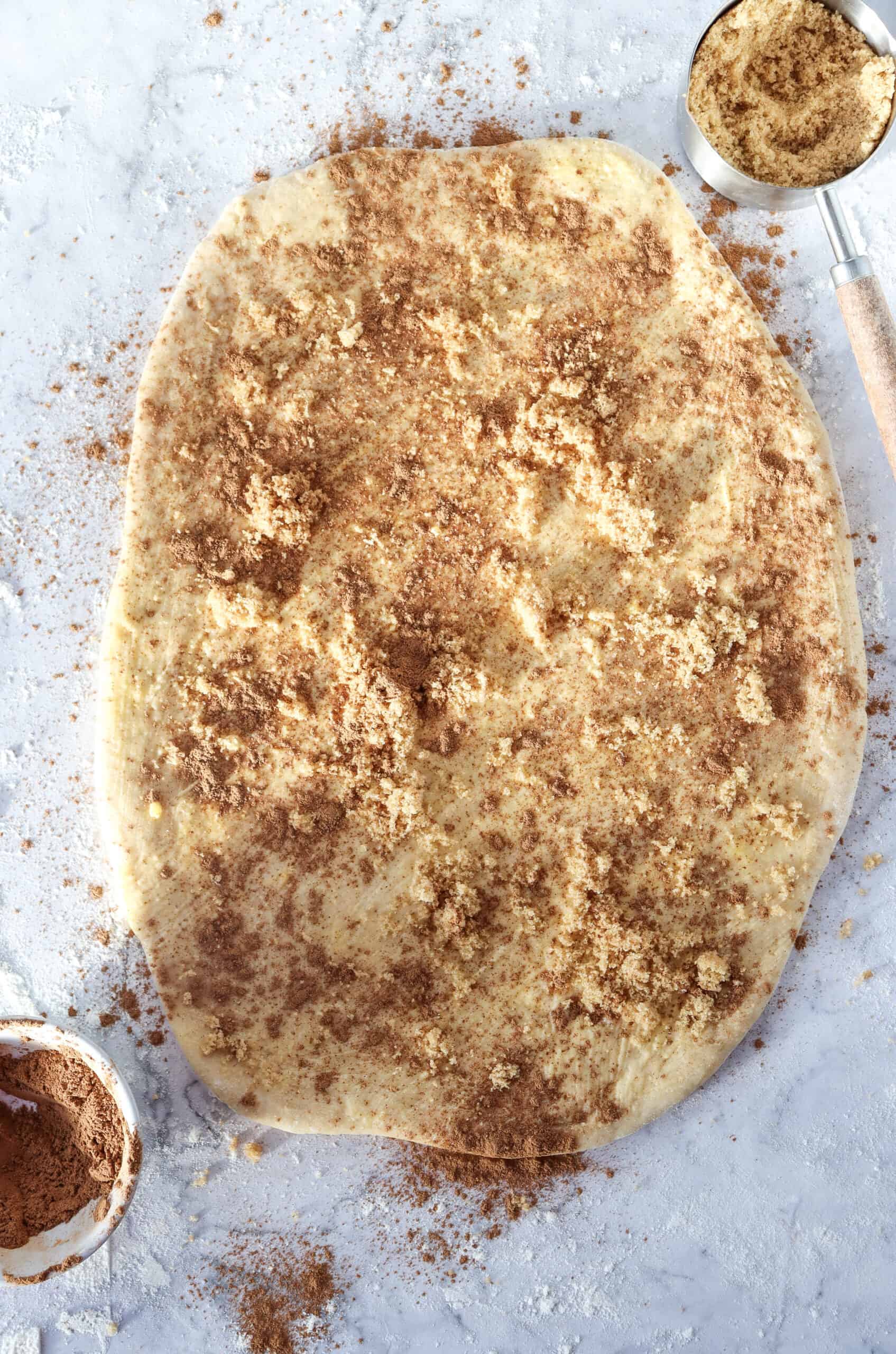 Cinnamon-sugar filling being evenly spread over the rolled-out dough.