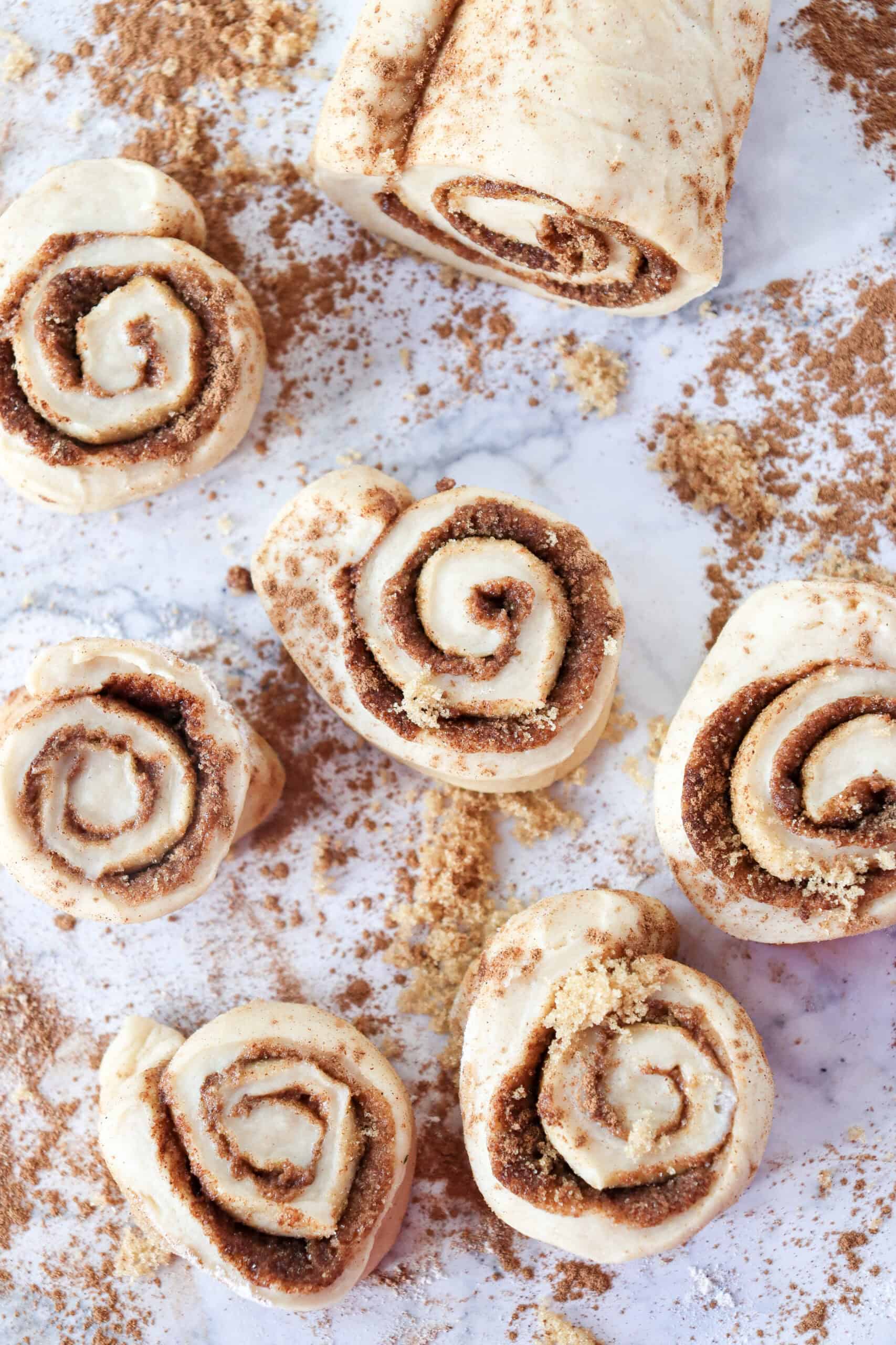 Overhead view of six sliced cinnamon rolls next to the remaining log of dough with filling.