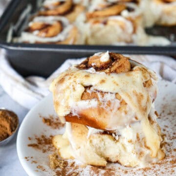 A stack of two cinnamon roll pieces on a plate, with the square pan of remaining rolls in the background.