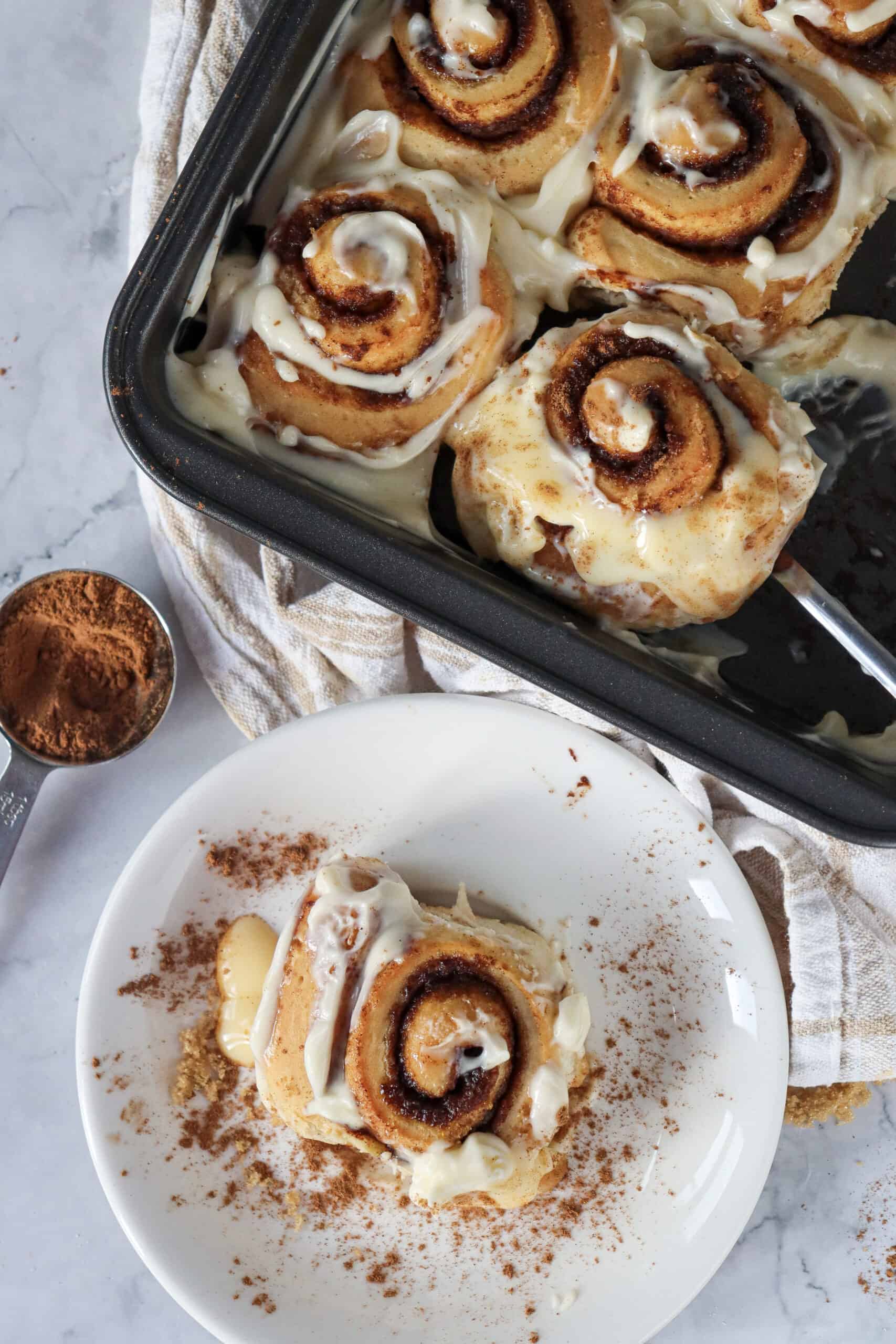 Overhead view of a stack of two cinnamon roll pieces on a plate, with the square pan of remaining rolls nearby.