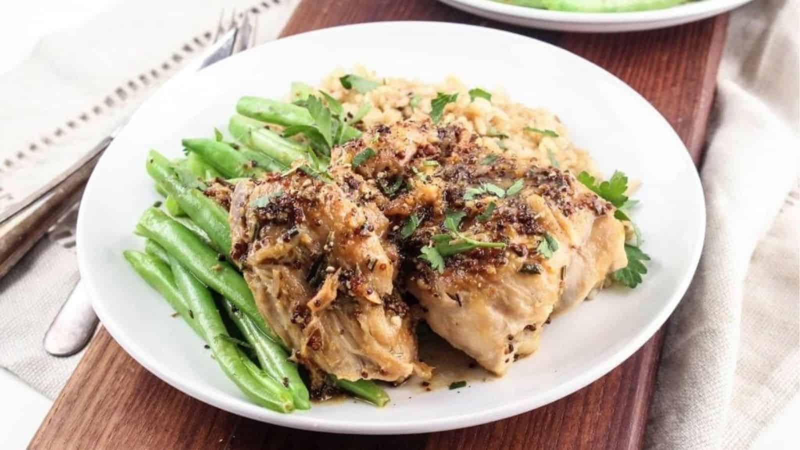 Chicken thighs with mustard sauce on top next to green beans on a white plate.