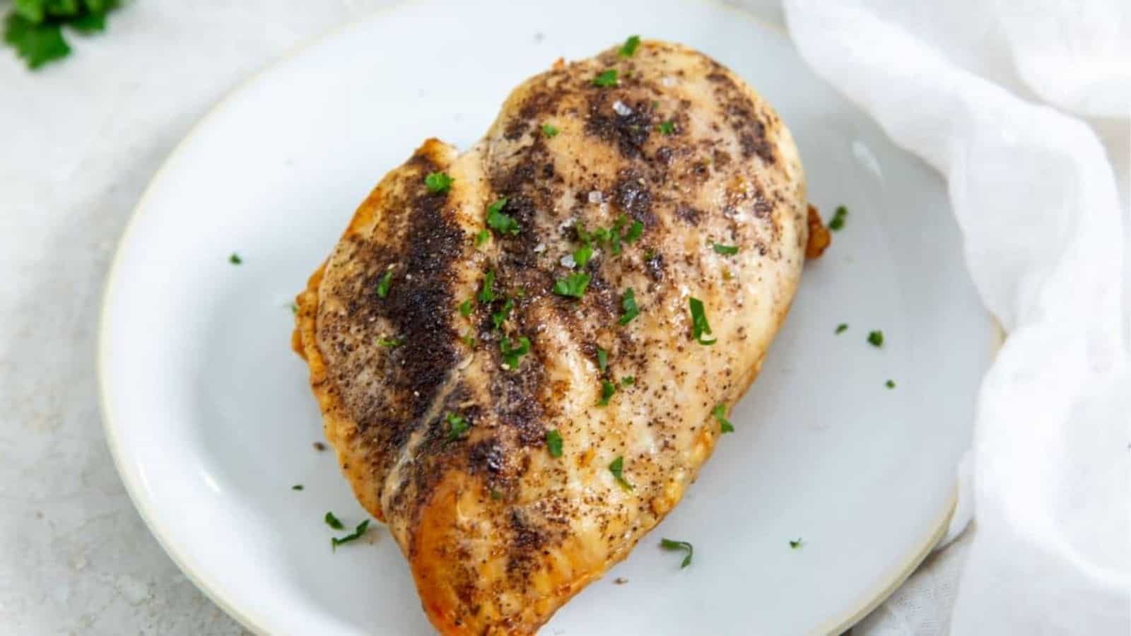 Juicy Air Fryer Boneless Skinless Chicken Breast on a white plate with parsley, onions, and tomatoes.