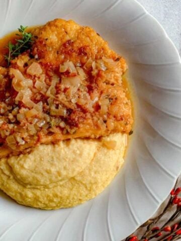 A pan-fried chicken cutlet with apple cider sauce and shallots on a plate.