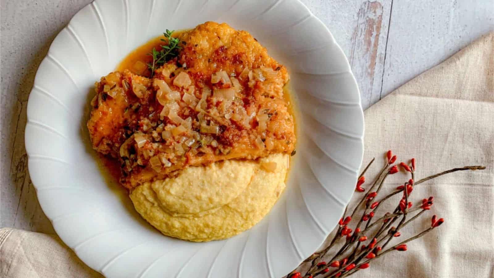 A pan-fried chicken cutlet with apple cider sauce and shallots on a plate.