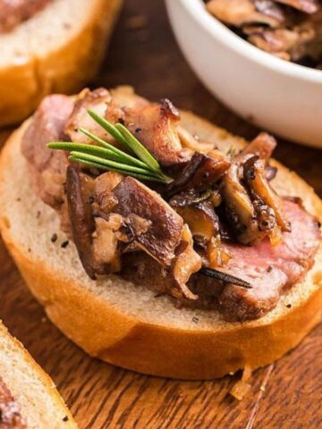 Close-up image of steak and shitake mushroom crostini appetizers on a wooden surface.