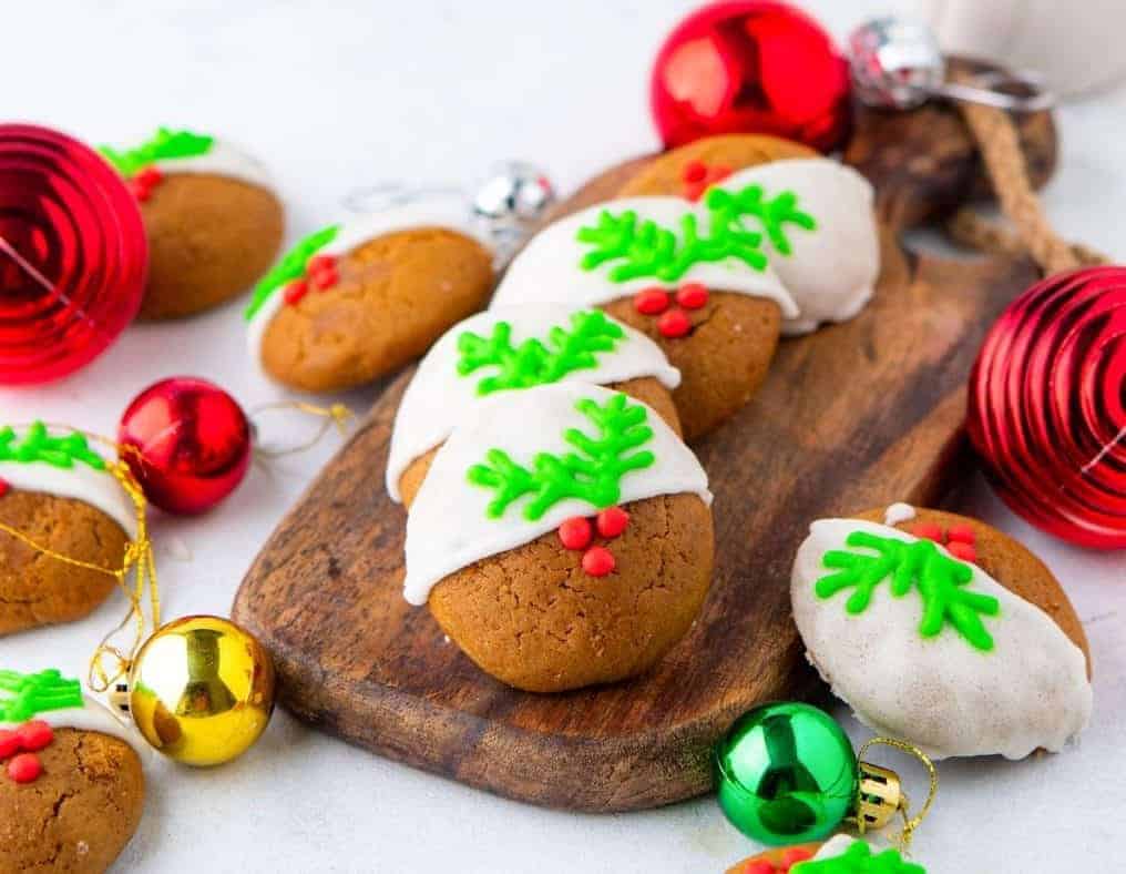Gingerbread cookies with christmas decorations on a wooden cutting board.