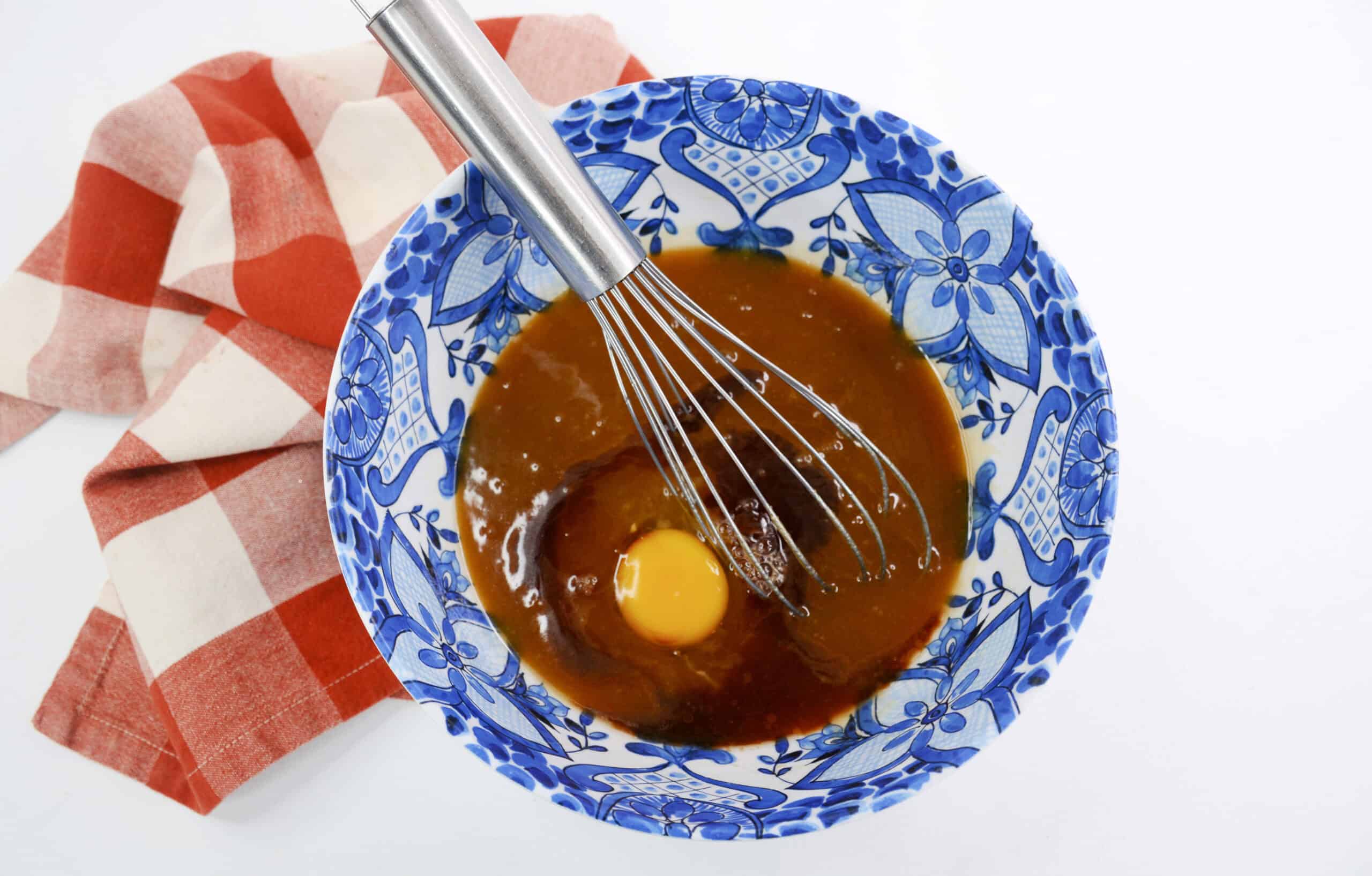 Overhead image of eggs and vanilla added to the mixture with a whisk in a bowl.