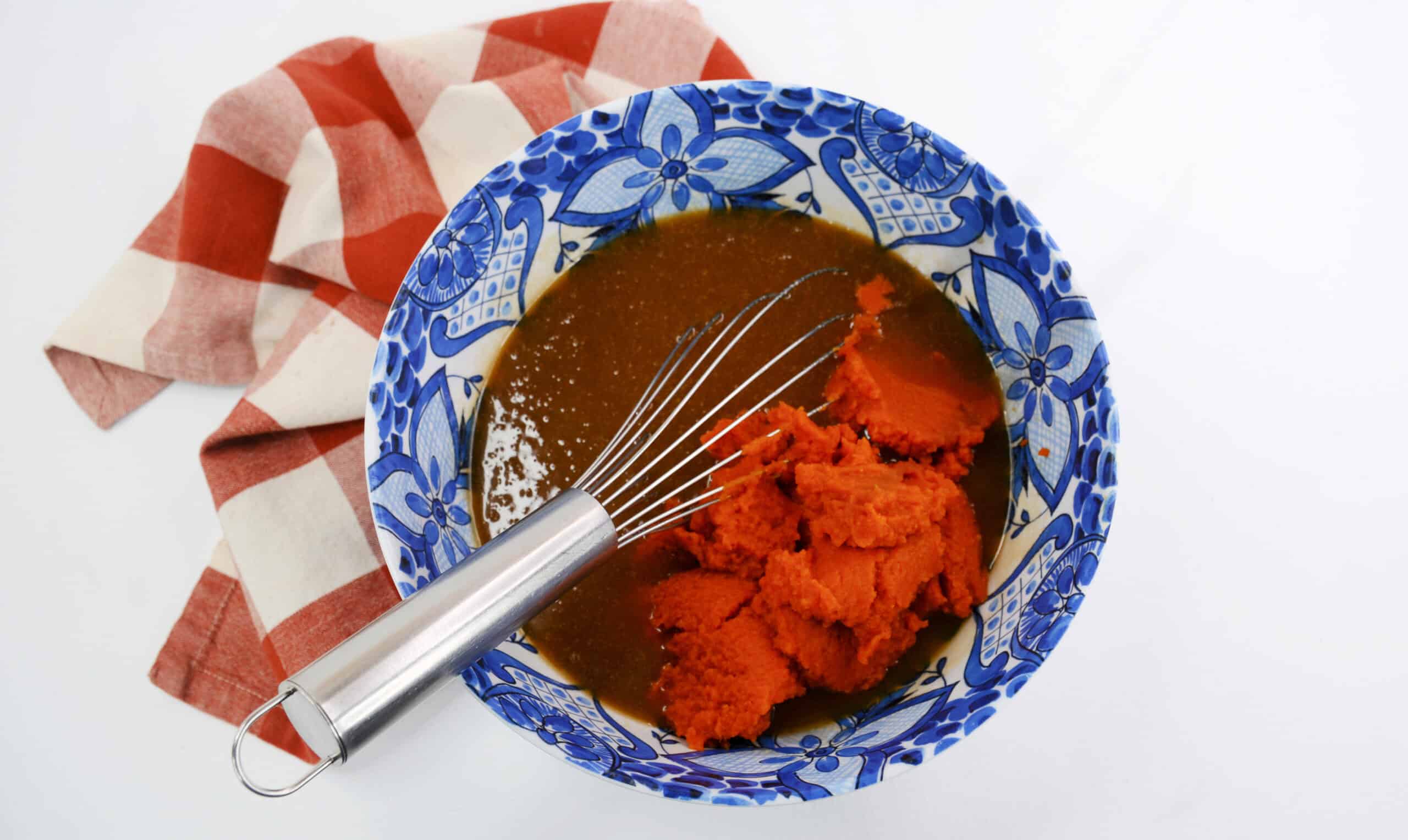 Close-up image of pumpkin purée added to the wet ingredients with a whisk in a bowl.