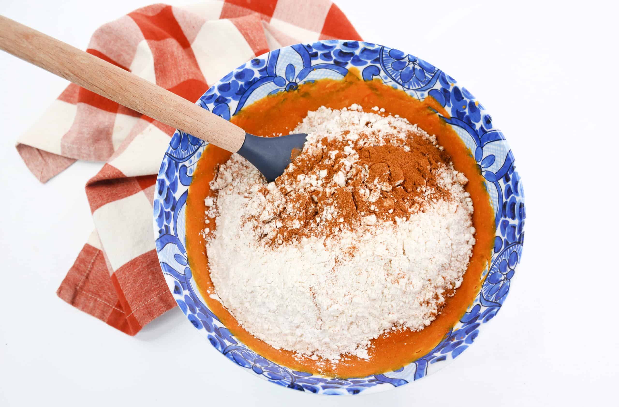 Overhead image of dry ingredients on top of wet ingredients with a spatula in a mixing bowl.