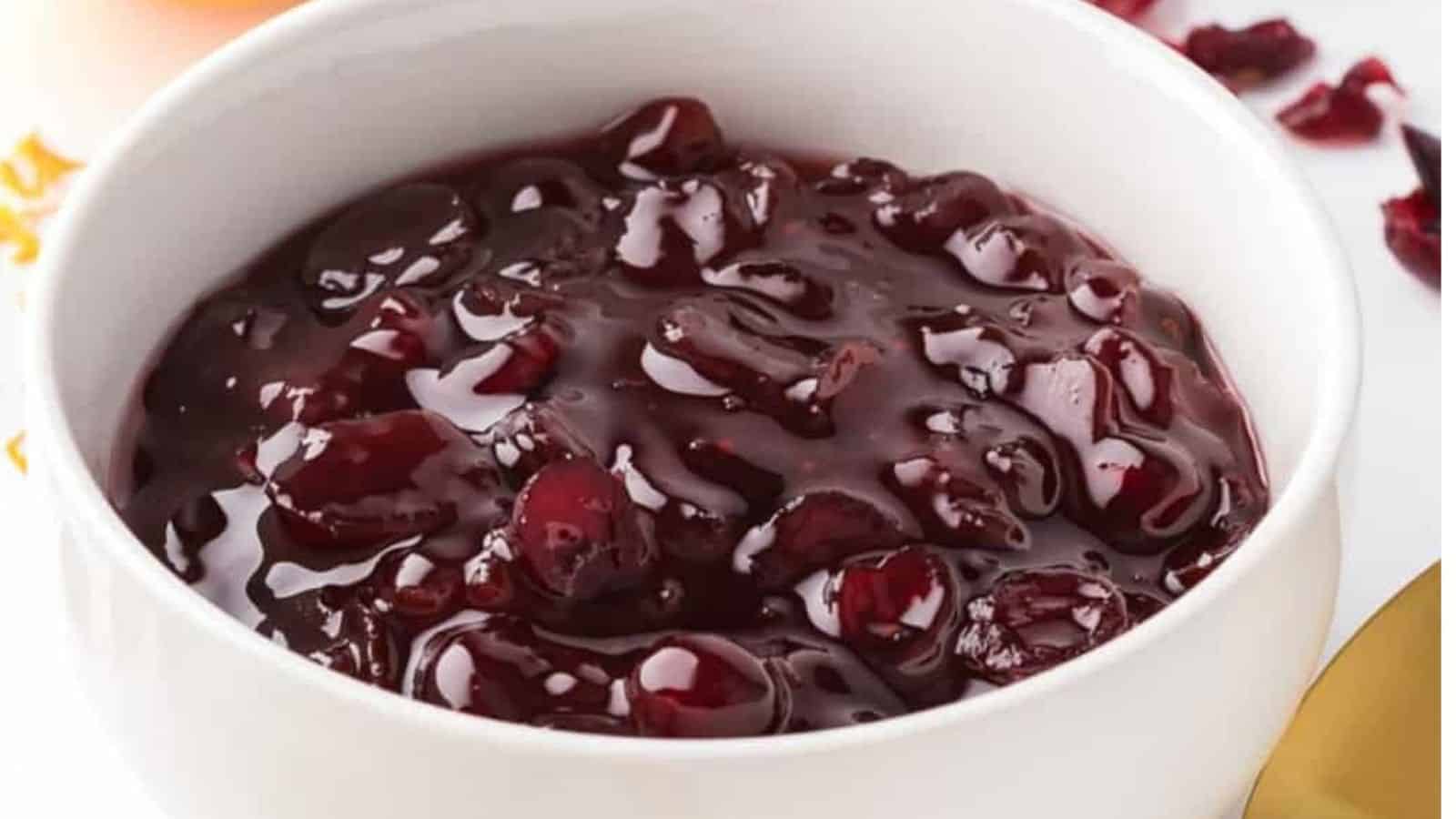 Close up view of cranberry sauce in white bowl with oranges in the background