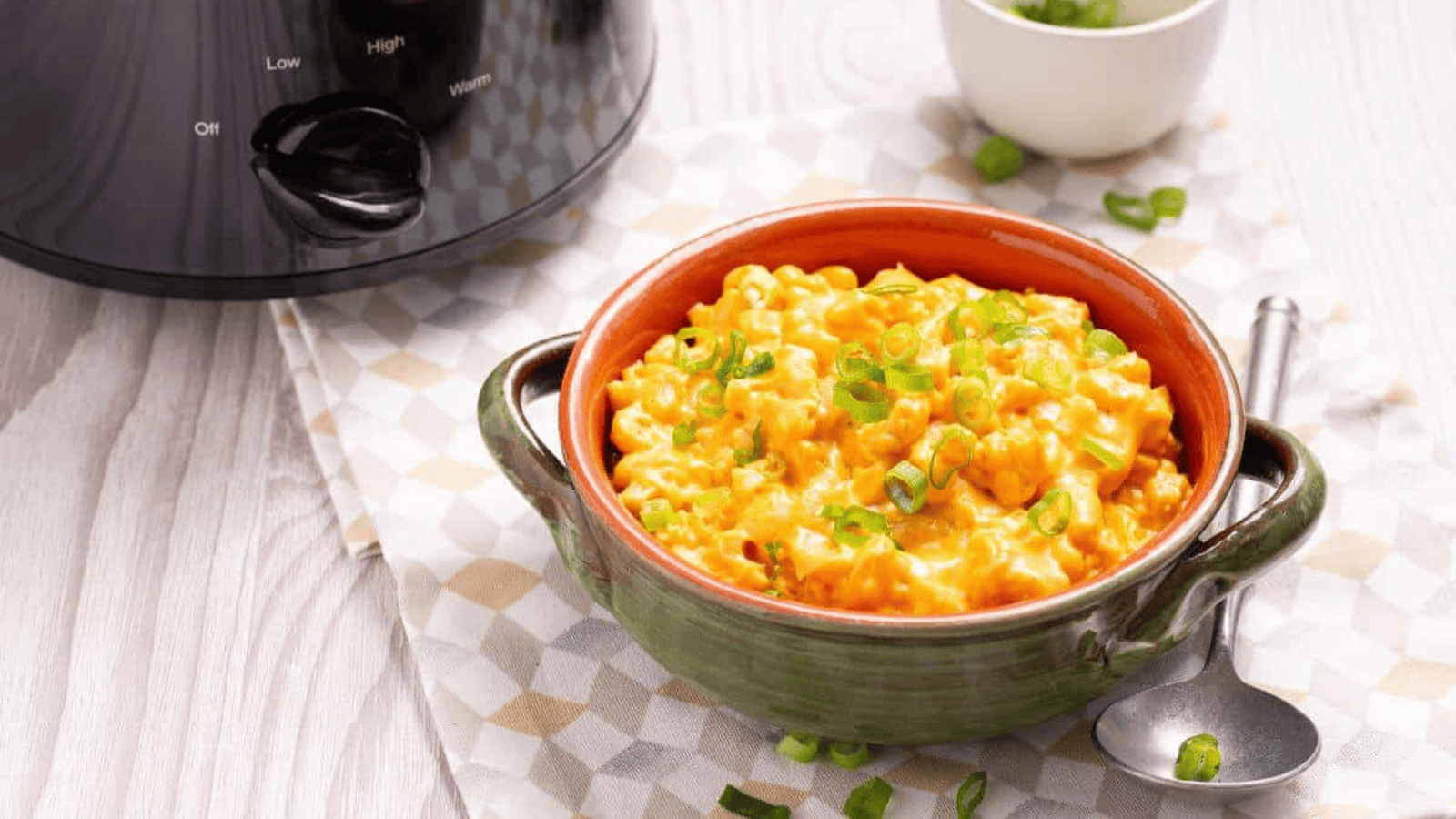 A bowl of macaroni and cheese in front of a slow cooker.