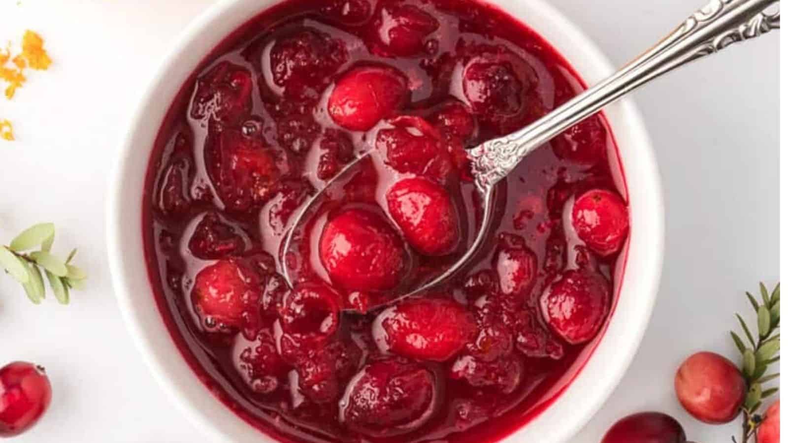 Close up shot of cranberry sauce in white ramekin with a spoon in it.