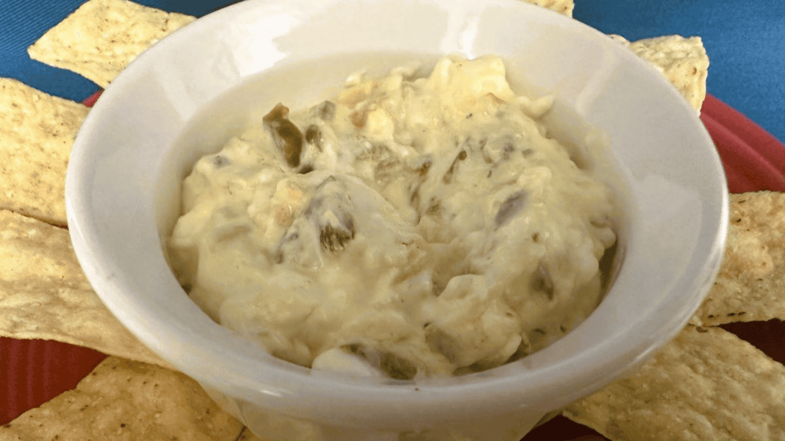 A white bowl of dip with chips and cheese.