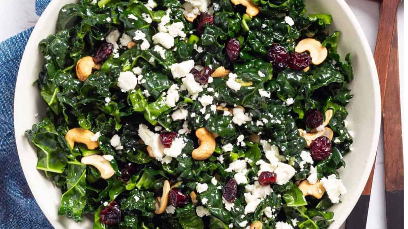 An overhead image of kale salad with cranberries, toasted cashews, and topped with goat cheese