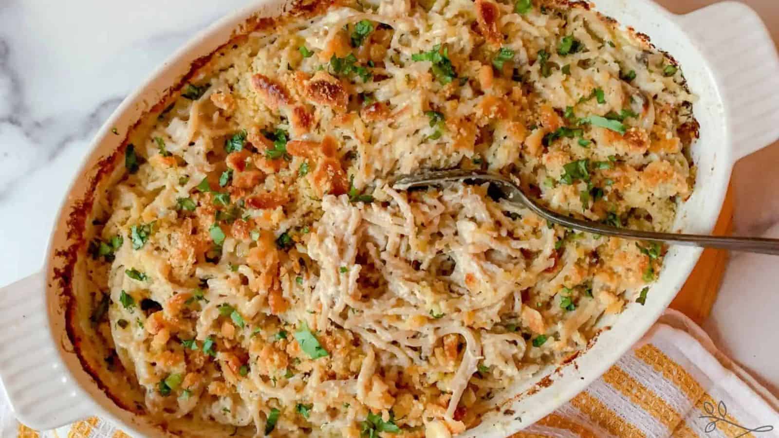 A casserole of turkey and noodles tetrazzini with a serving spoon resting in the center.