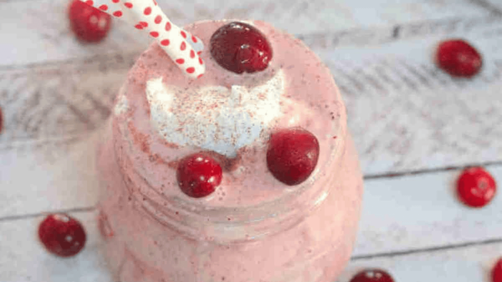 Apple cranberry smoothie i a mason jar with whole30 whipped cream and cranberries on top and cranberries around the jar and straws in it.