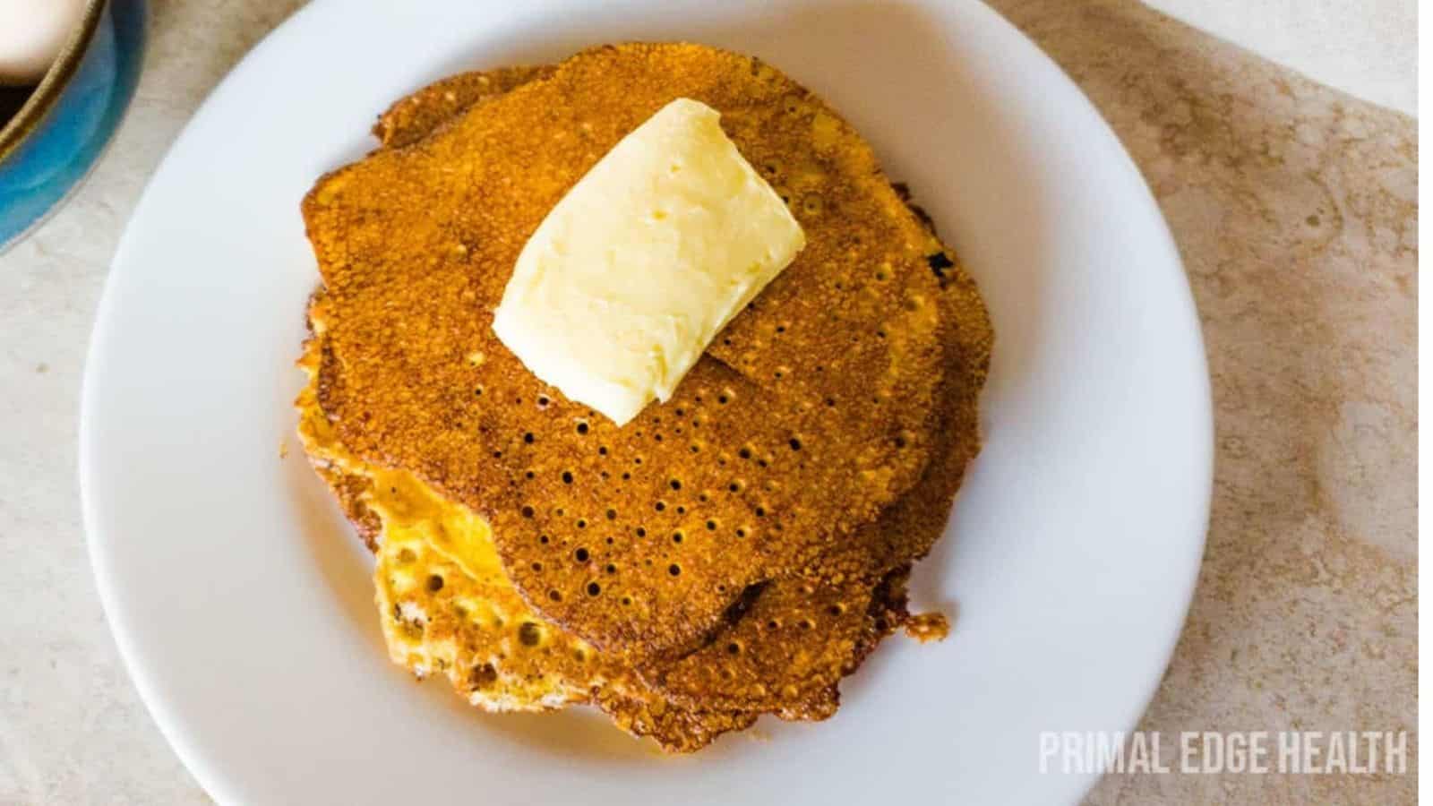 A stack of cream cheese pancakes on white plate with butter.
