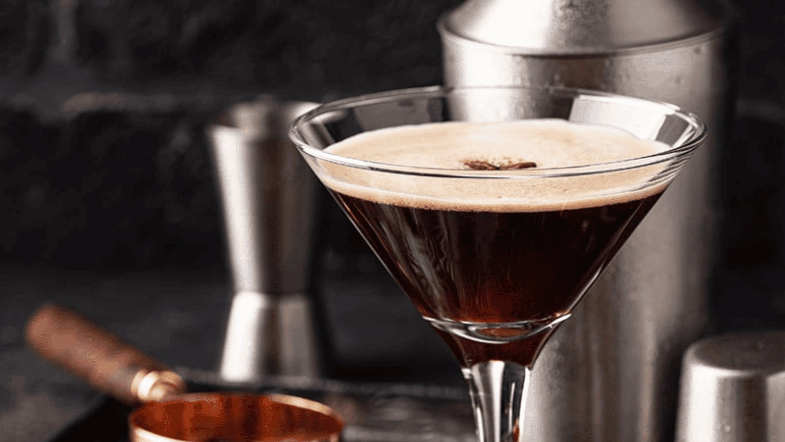 keto espresso martini in martini glass with shaker and bar items in background.