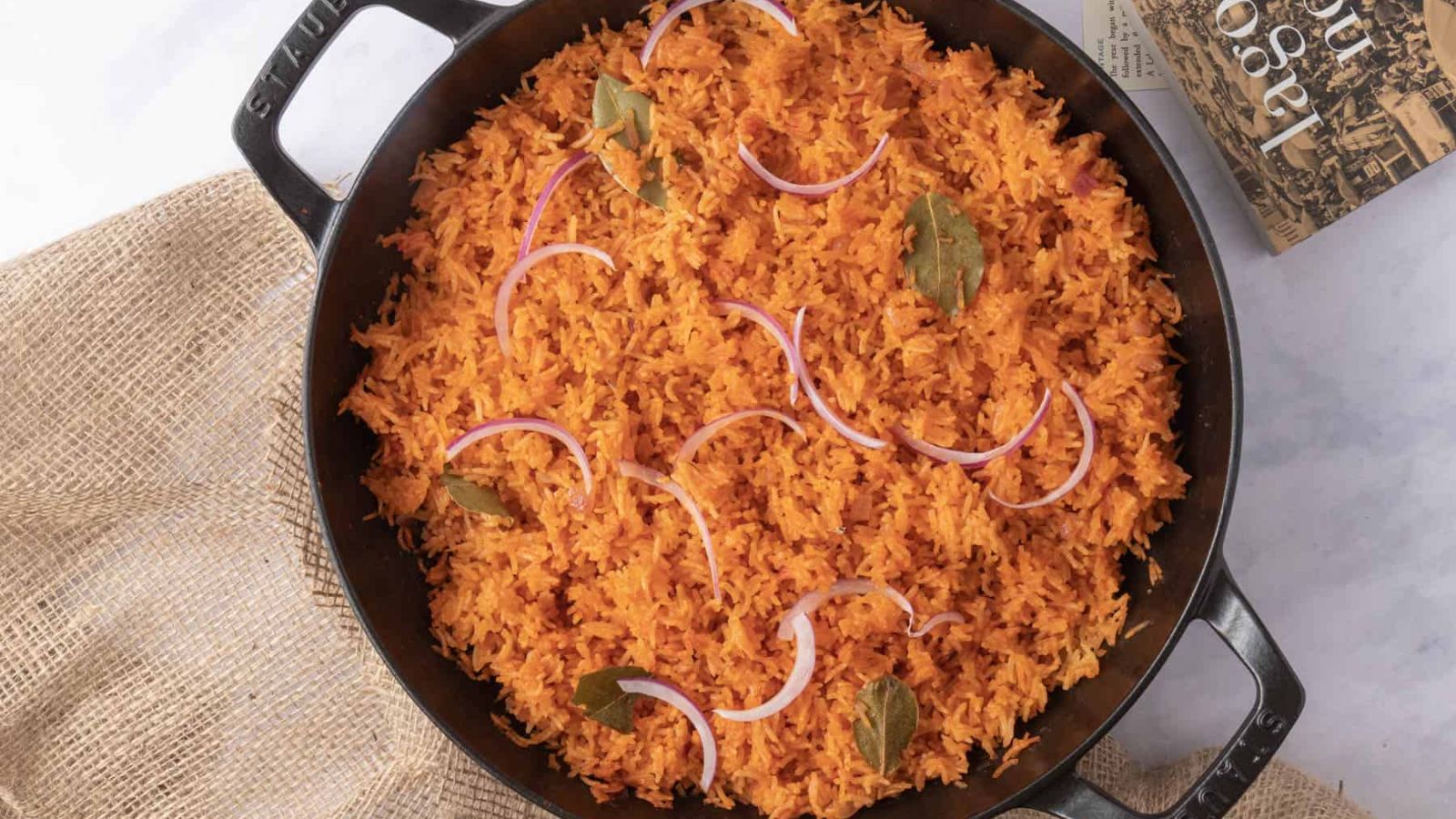A close up image of nigerian jolloff rice garnished with slices of red onion and bay leaves.