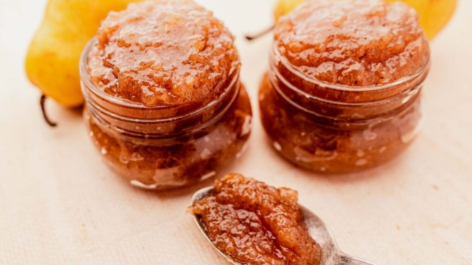 Close-up image of two jars and a spoon full of pear jam.