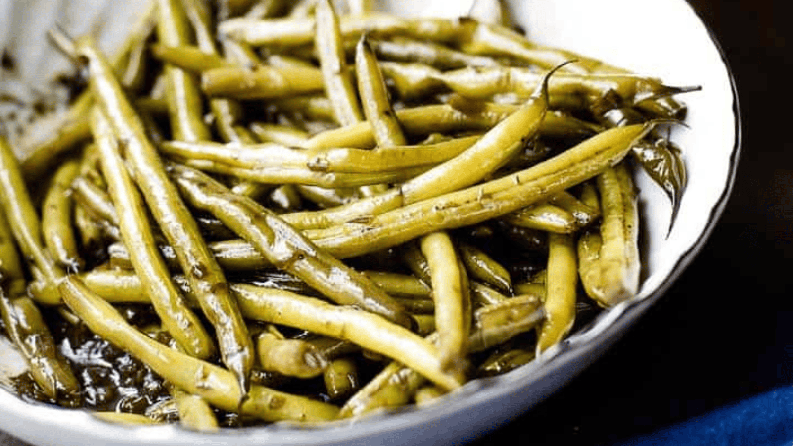 Overhead shot of worcestershire green beans in a white serving bowl next to a blue towel.