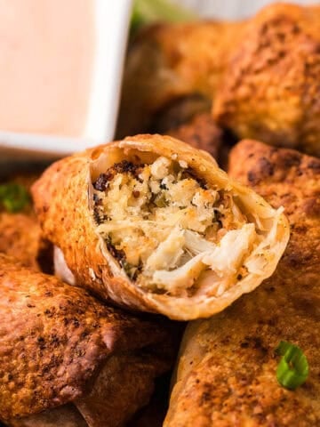 A close-up image of a stack of Air Fryer Crab Cake Egg Rolls with a dip on the background.