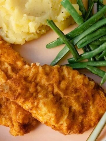 Fried chicken with mashed potatoes and green beans on a plate with a fork.