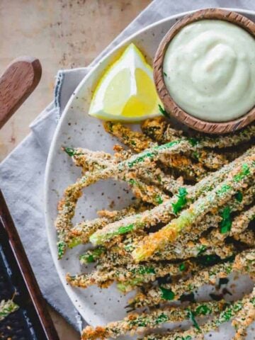An overview of Crispy Baked Asparagus Fries on a plate with a slice of lemon and a dip.