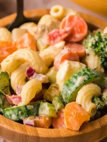 A wooden bowl filled with Garden Veggie Macaroni Salad and Creamy Avocado Dressing.