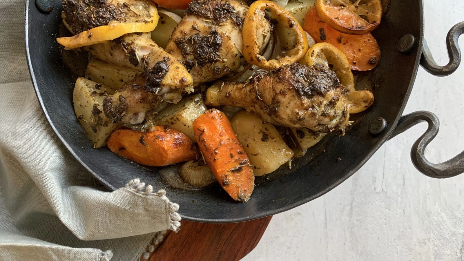 An iron skillet filled with hot chicken drumsticks and potatoes and carrots.