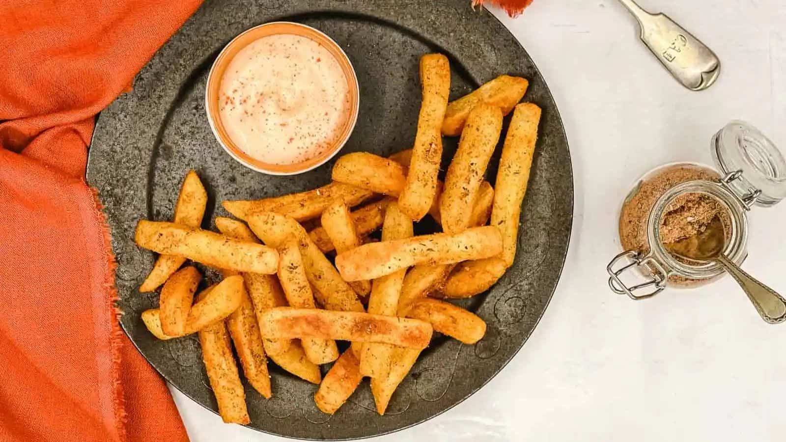 Top view of Peri Peri Fries and a dip on a black plate.