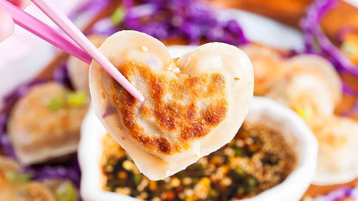 Someone holding a Pork Potsticker with a pair of chopsticks.