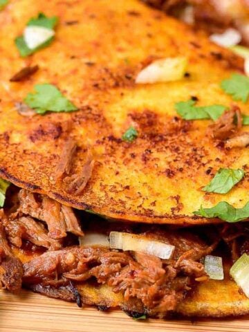 Overhead shot of quesabirria tacos with lime wedges.