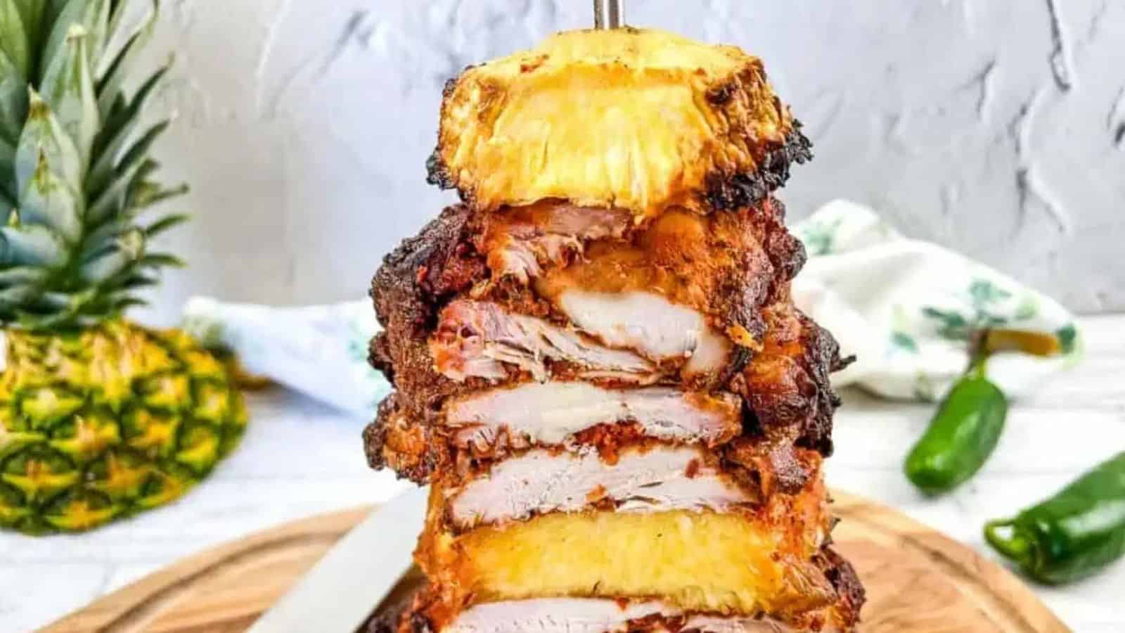 A stack of chicken and pineapple on a vertical skewer on a cutting board.