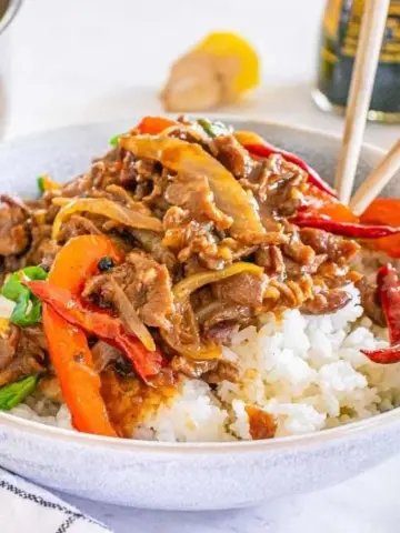 A bowl of Szechuan Beef on top of rice.