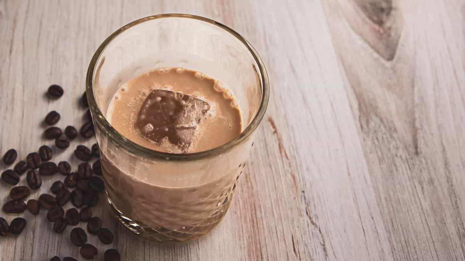 A glass of White Russian Mocktail with ice and some beans on the side.