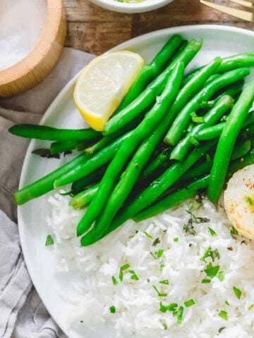 A plate of rice with Air Fryer Scallops, some green beans, and slices of lemon.