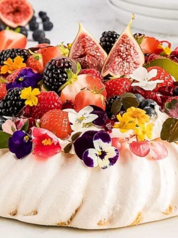 An image of a pavlova topped with fresh berries, figs, and edible flowers.