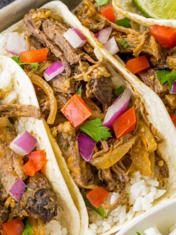 Barbacoa tacos on a tray topped with peppers and onions.