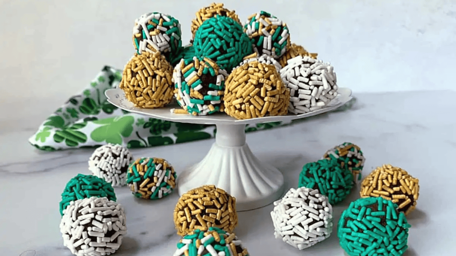 Green, gold and white sprinkle covered truffles on a white pedestal.