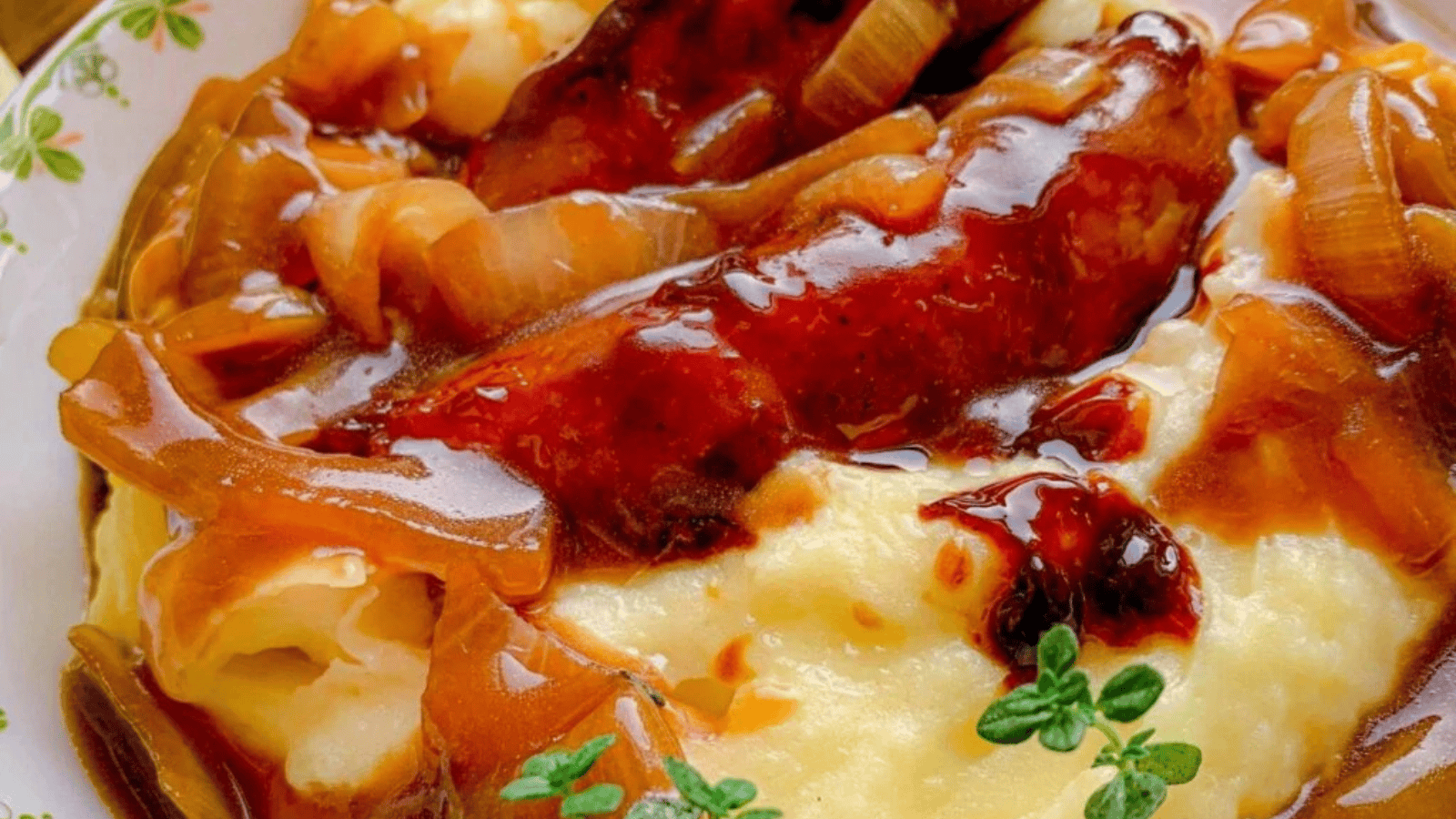 A bowl brimming with pork sausages over a thick bed of mashed potatoes that are smothered in onion gravy.