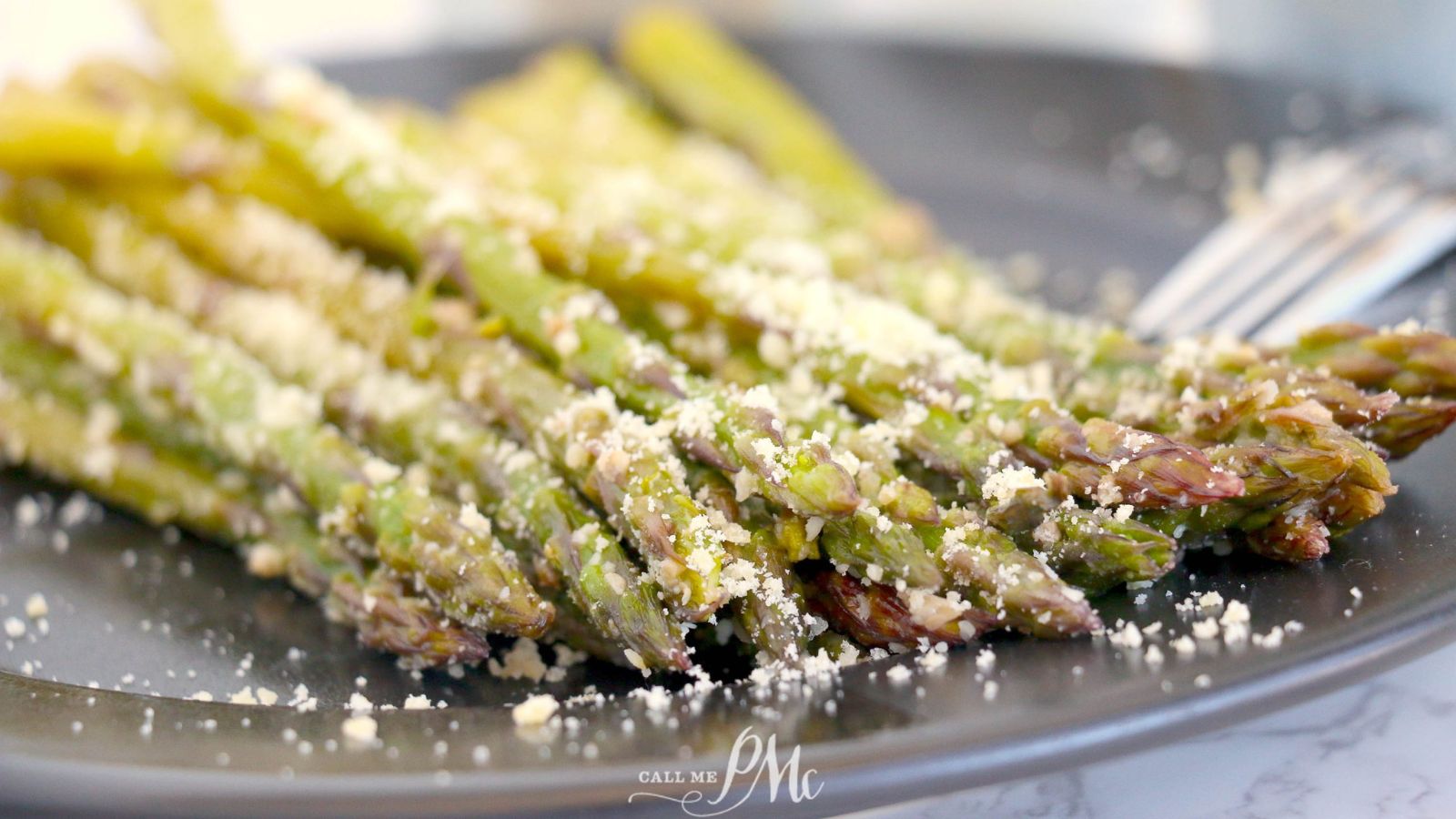 Asparagus on a black plate with parmesan cheese.