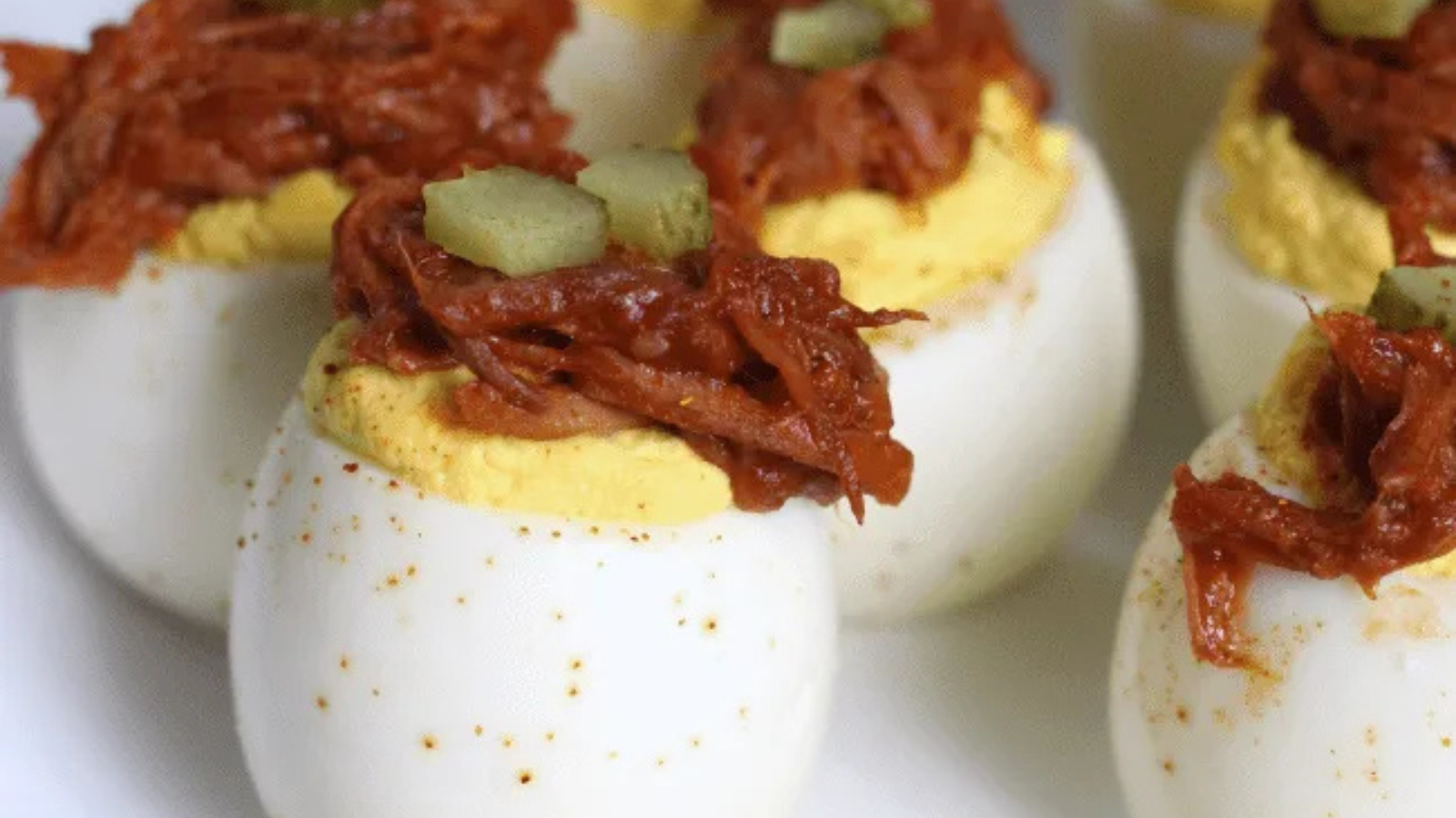 Blue plate with pulled pork deviled eggs, all topped with a pickle.