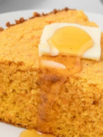 An image of a slice of sweet potato cornbread on a plate with butter and honey on top.