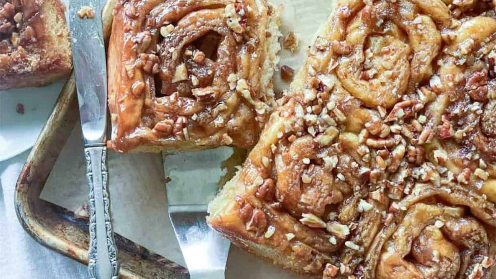 Close-up image of apple cinnamon rolls with pecans on a baking sheet.
