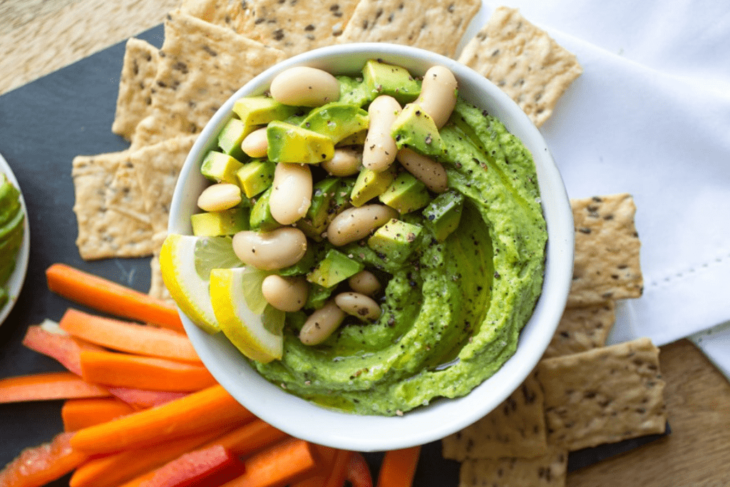 Avocado hummus in a bowl with white beans, diced avocado, and lemon slices.