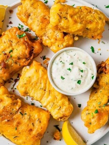 A plate of Beer Battered Fish with slices of lemon and a dip.