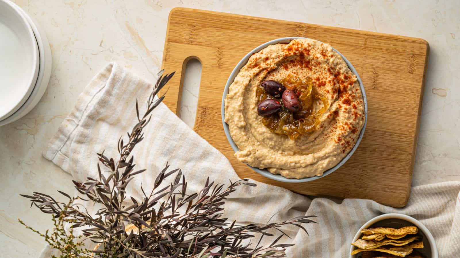 An overview of a bowl of Caramelized Onion Hummus on a wooden board.